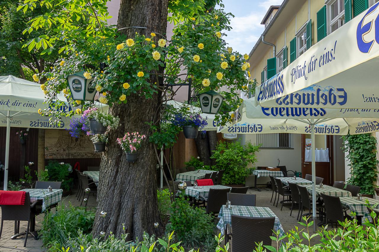 Schattiger Gastgarten des Brandhof mit Blumen und Tischen